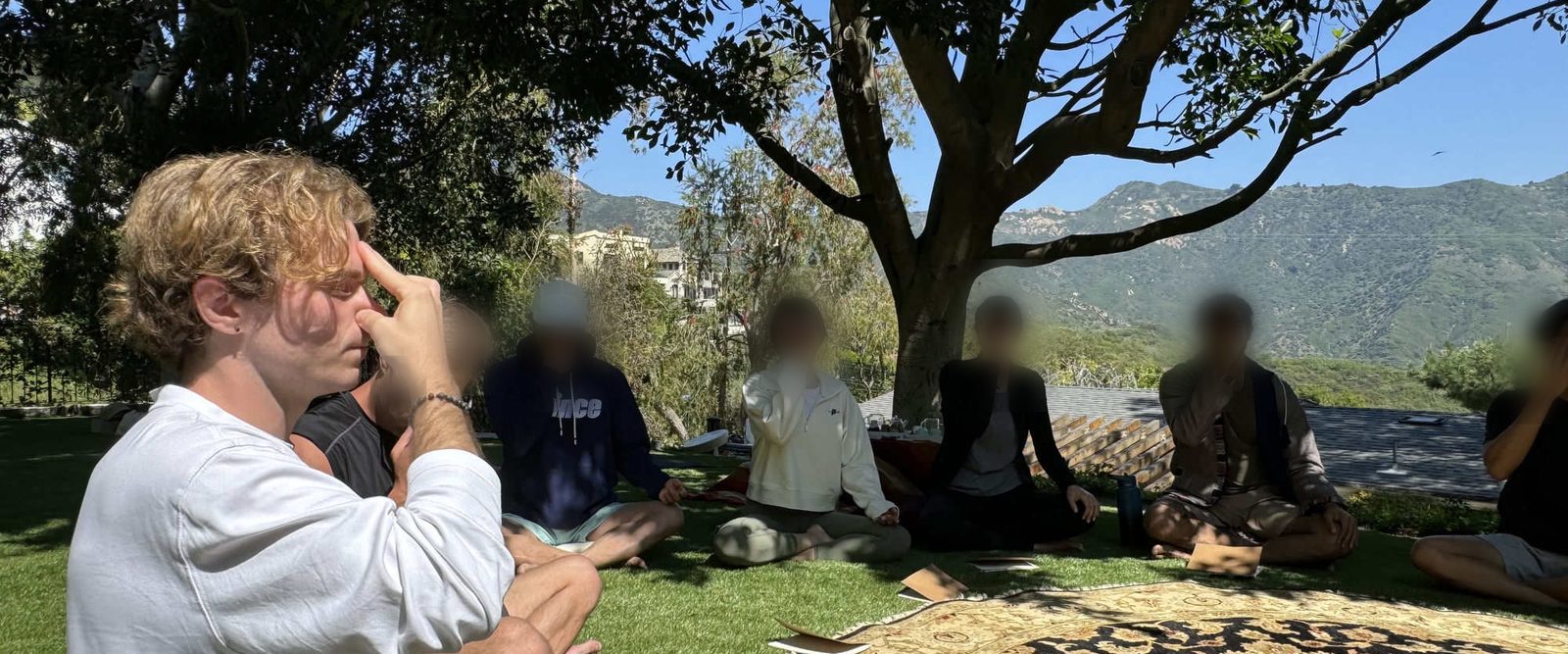Xander leading a group breathwork circle outdoors, everyone seated with eyes closed