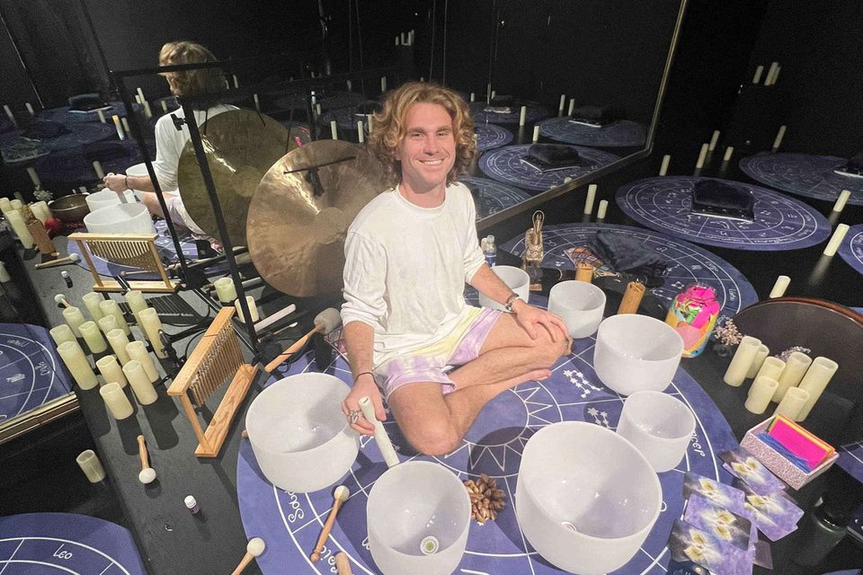 Xander seated among crystal singing bowls, gongs and candles in a darkened studio